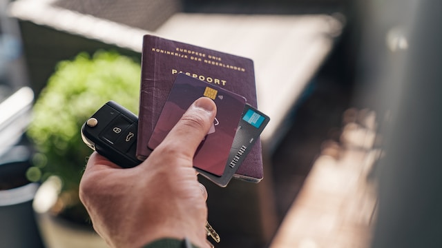 Hand holding a car key, passport and credit cards.